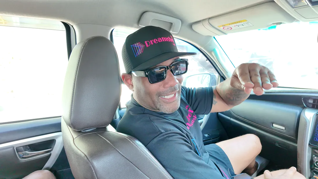 A client in a cap and sunglasses laughing in the front seat of a car during a shoot