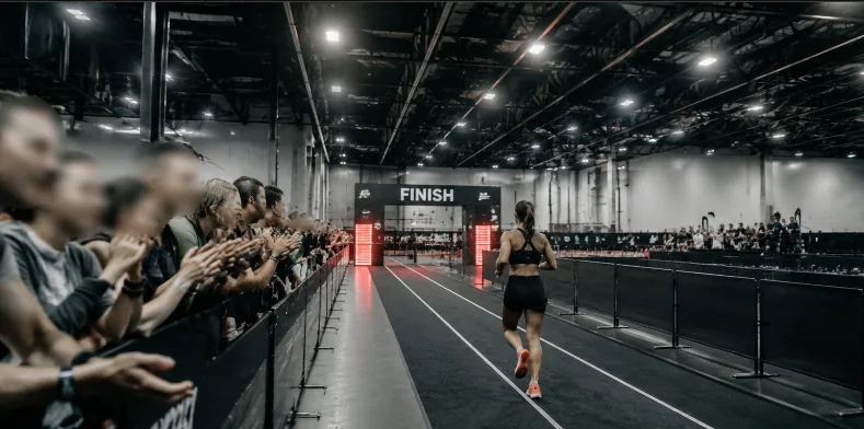 An athlete crossing the HYROX finish line in Bangkok as the crowd applauds from behind the barrier