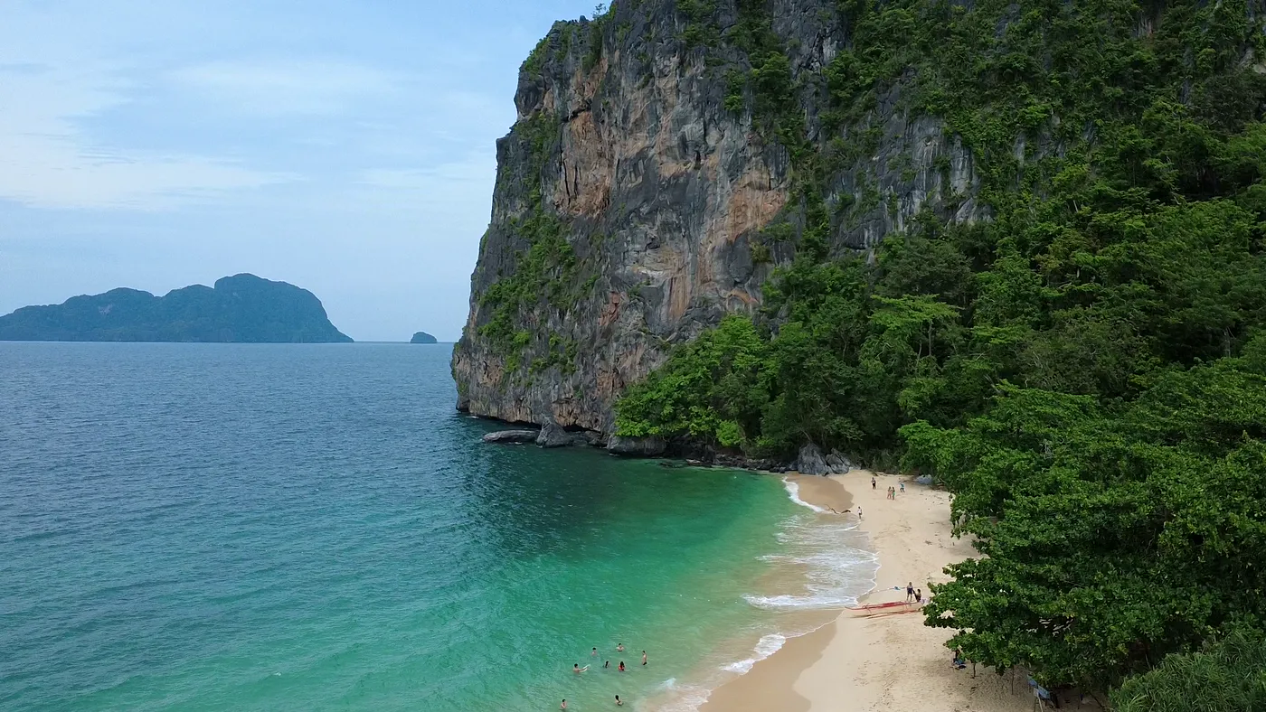 Aerial of a towering limestone cliff above a turquoise beach, Palawan