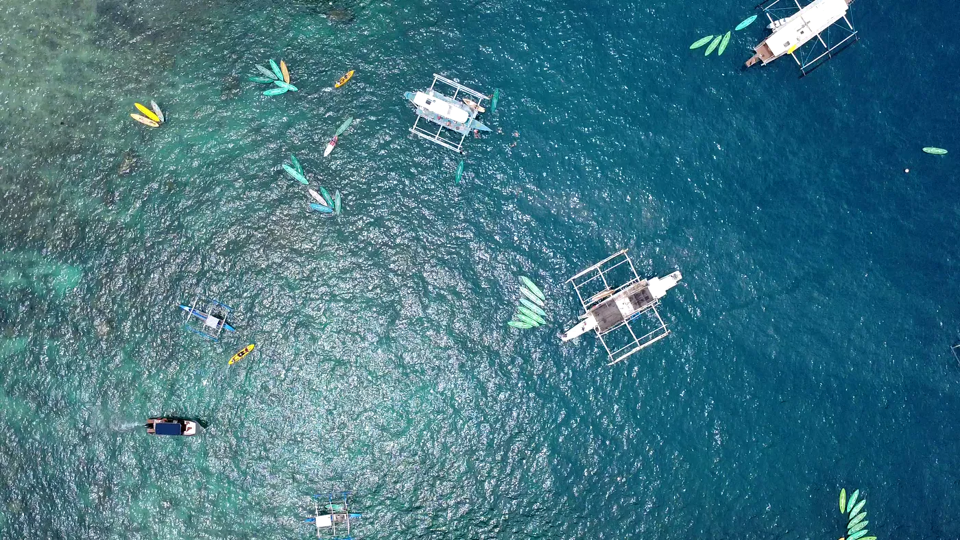 Top-down aerial of boats, kayaks and swimmers over a shallow reef, Palawan